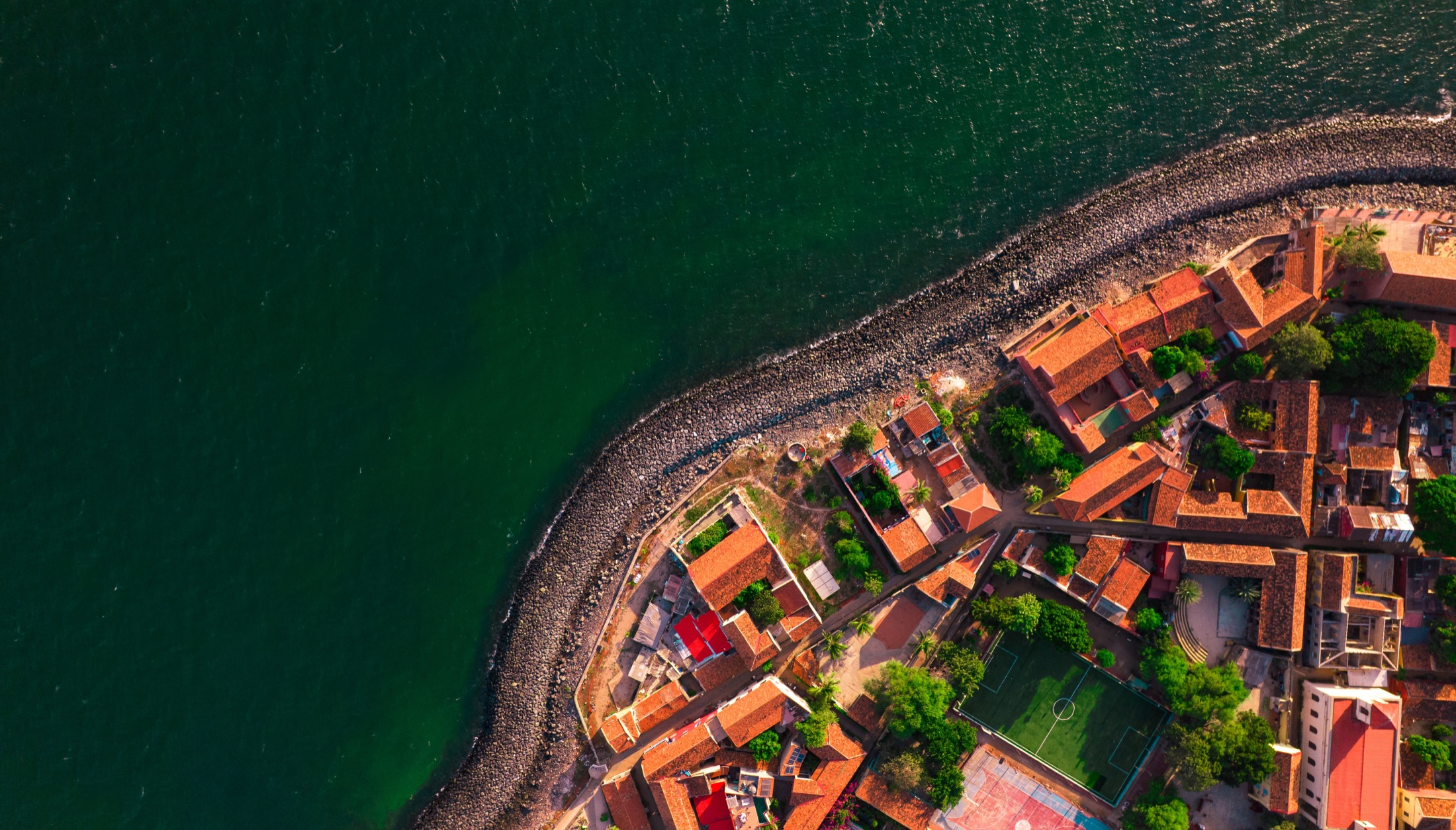 Aerial view of Goree Island with red rooftops and dark green ocean